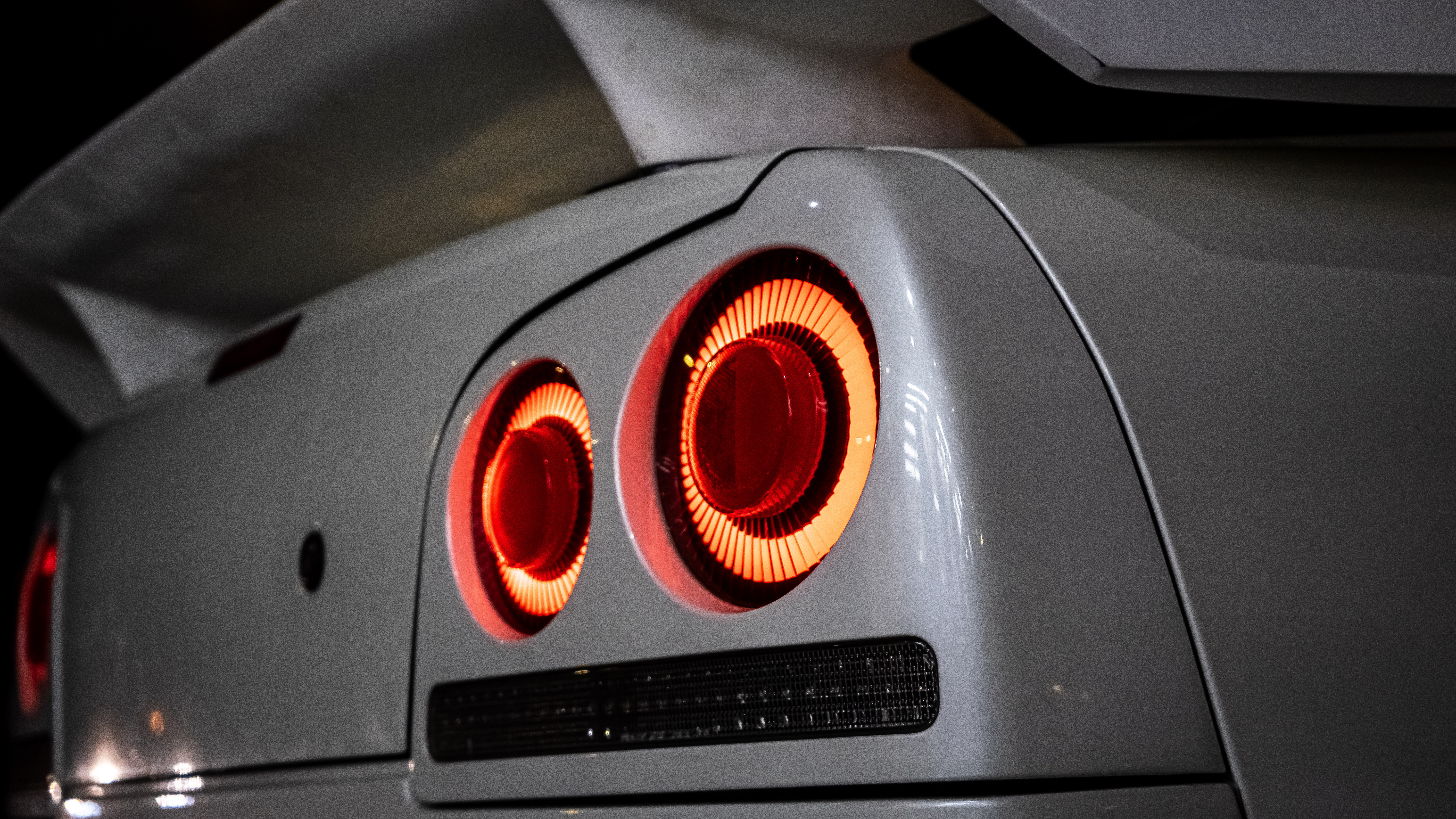 Close-up of glowing red round taillights on a Nissan Skyline R34 against a dark background